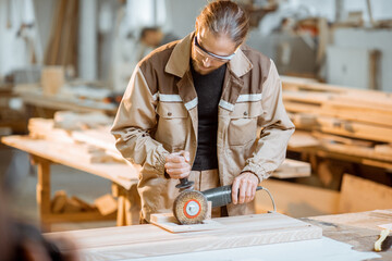 Wall Mural - Handsome carpenter in uniform brushing wood with hand machine at the carpentry manufacturing