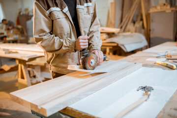 Wall Mural - Handsome carpenter in uniform brushing wood with hand machine at the carpentry manufacturing