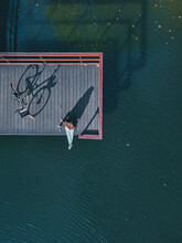 Aerial View Of Young Woman Sitting Alone At Edge Of Coastal Jetty