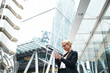 © PETE  MULLER/Westend61 - Beautiful female professional using smart phone while standing against office building at downtown district