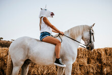 Young Woman Wearing Unicorn Mask Sitting On Horseback