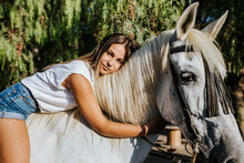 Portrait Of Beautiful Young Woman Leaning On Top Of White Horse