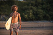 © SERGIO NIEVAS/Westend61 - Shirtless young man with surfboard looking away while walking at beach during sunset