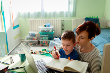 Wall Mural - Mother using laptop teaching with her son online at home in his room.