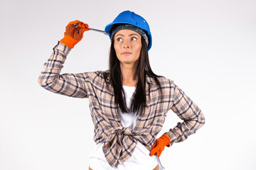 Female mechanic wearing blue hard hat holds a wrench and looks thoughtfully to the side. White background.