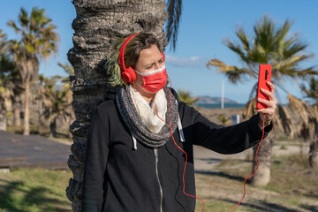 Sticker - Shot of a woman in a protective mask with headphones talking by phone           - new normal