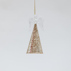 Poster - Christmas toy in the shape of a fragile angel in a golden shiny skirt on the light background