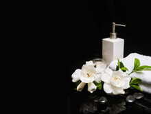 Beautiful Spa Concept Of Two White Gardenia Flower And Green Leaf And Towel, Candle,oil Bottle  On Pile Of Black Zen Stones 