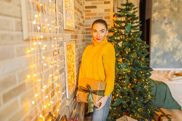 Wall Mural - Beautiful cheerful happy young girl with christmas gifts on the background of a new year tree at home