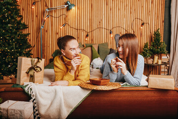 Wall Mural - Two beautiful cheerful happy young girls girlfriend give Christmas gifts on the background of a new year tree at home