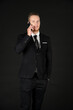 © Arunporn - Portrait of young smart confident and successful businessman in black suit using smartphone isolated on black background