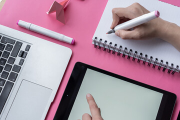 Wall Mural - Hand holding marker with a notebook, tablet, laptop, and swan origami on pink background