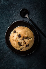 Wall Mural - Fresh chocolate chip muffin on black plate. Top view