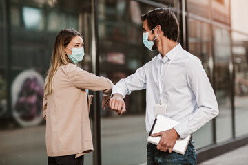 Business man and woman with safety masks greeting with elbow bump in front of office building.