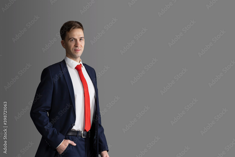 Photo Stock handsome, attractive man in blue suit and red tie on grey  background. confident, serious businessman, lawyer with hand in his pants  in pocket and smiling. business. copy space | Adobe