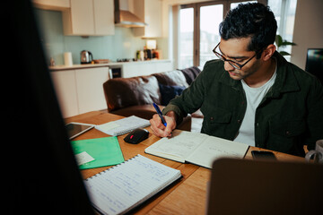 Wall Mural - mixed race businessman writing in note pad working from desktop computer 