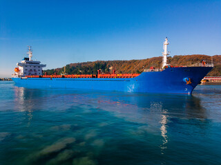 A blue ship in the seaport on a sunny day under a blue cloudless sky with a mountain in the distance.