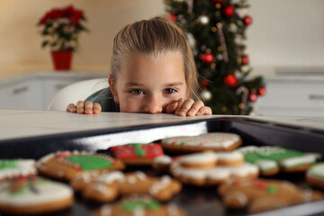 Wall Mural - Cute little girl near baking sheet with fresh Christmas gingerbread cookies indoors