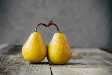 A couple of Fresh yellow ripe organic yellow pears form the shape of the heart on rustic wooden table on the gray stone background. Relations, love concept. Trend Colors of the year 2021. Copy space.