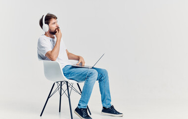 Poster - man in headphones with laptop on his knees sitting on chair communication isolated background