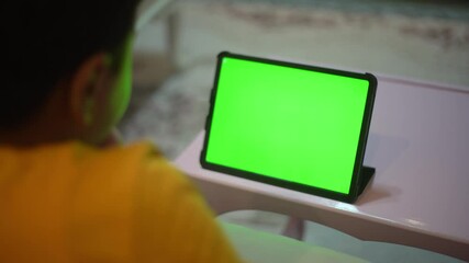 A teenage boy is watching a tablet green screen.