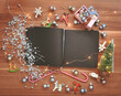 Top view of an empty pages black notebook surrounded with colorful Christmas ornaments and decorations and lights on a warm wooden background. Christmas wishes or happy holidays background. 