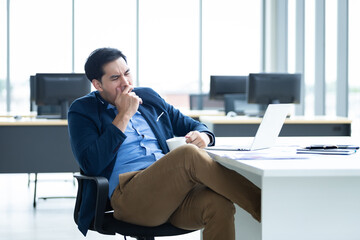 Asian young businessman bored yawning in front worked late and tired fell asleep or having stressful time on laptop computer In the office room background.