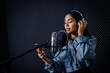 © Thinapob - Happy cheerful pretty smiling of portrait of young Asian woman look at the smartphone vocalist Wearing Headphones recording a song front of microphone in a professional studio