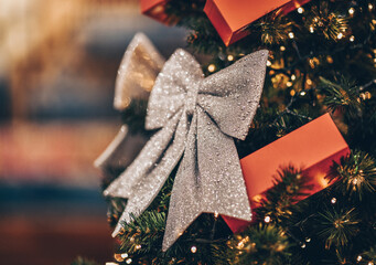 Wall Mural - Decorated Christmas or new year fir tree. Close-up on branches with lights and silver sparkling bows. Blurred fairy background