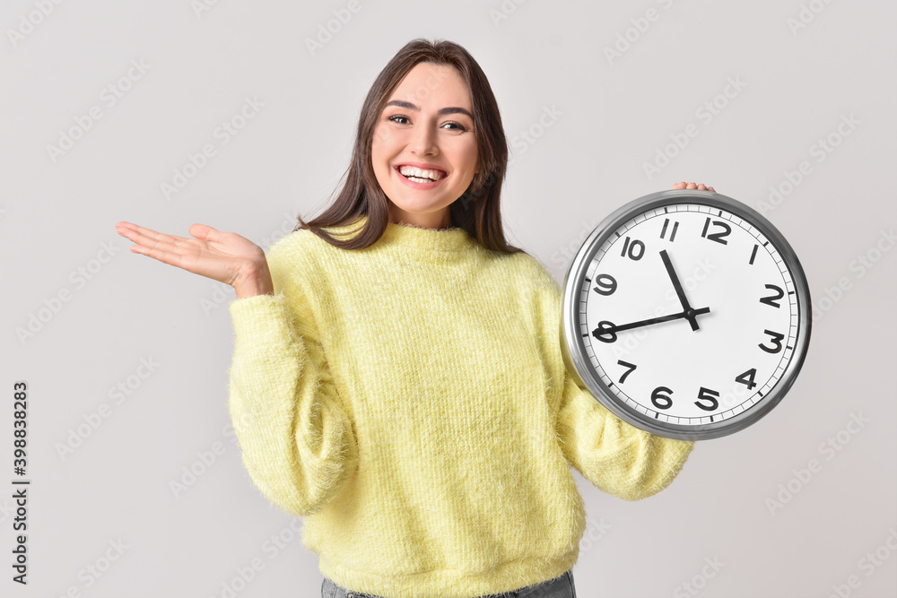 Beautiful young woman with clock on grey background