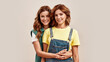 Portrait of two attractive young girls, twin sisters in casual wear smiling at camera, embracing, posing together, standing isolated over light background