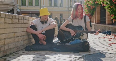 Wall Mural - Boy and teenage girl with an acoustic guitar on city street, girl playing the guitar singing with friend