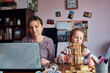 © Przemek Klos - Woman mother working doing her job remotely during video chat call stream online course webinar on laptop from home while her daughter playing with bricks toy. Woman sitting at desk