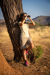 Canvas Print - Brunette stands leaning against tree using binoculars