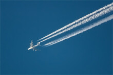 A huge four-engine wide-body passenger plane flies high in the sky and leaves a white contrail behind it.