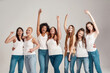 © Svitlana - Group of beautiful diverse young women wearing white shirt and denim jeans having fun, looking cheerful while posing together isolated over grey background