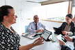 © SebastianCava - three women girls in bright office with large windows doing business at work meeting happy smile with laptop, ipad, folios and pens on the table