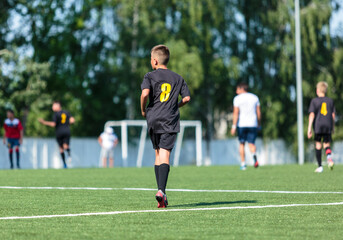 Wall Mural - Boys in black sportswear plays football on field, dribbles ball. Young soccer players with ball on green grass. Training, football, active lifestyle for kids