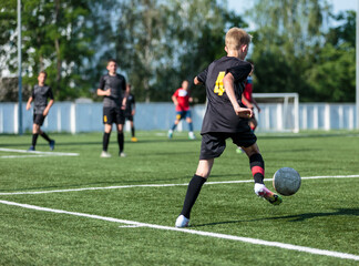 Wall Mural - Boys in black sportswear plays football on field, dribbles ball. Young soccer players with ball on green grass. Training, football, active lifestyle for kids