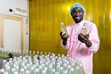 Wall Mural - African male factory worker holding a green juice bottle or basil seed drink in beverage factory