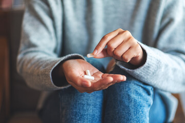 Closeup image of a woman holding and picking white medicine capsules in hand