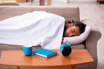 Wall Mural - Young man lying on the sofa in time management concept