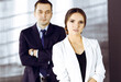 © cameravit - Young beautiful businesswoman is standing in an office with a male colleague at the background. Concept of success in a business