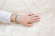 © fotoduets - Young adult woman hand touching white fluffy fur blanket. Flower bracelet on female wrist. Closeup. Top down view.