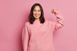 © WHstudio Leushin N - Powerful cheerful brunette woman raises arm and shows muscle demonstrates her strength looks confident at camera smiles gently wears casual long sleeved jumper isolated over pink background.
