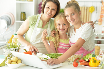 Wall Mural - Cute girls with mother preparing delicious fresh salad in kitchen