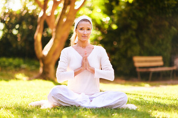Wall Mural - Beautiful mature woman meditating in green sunny garden or park, healthy lifestyle
