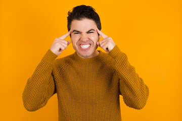 Wall Mural - Young handsome Caucasian man wearing yellow sweater against orange wall concentrating hard on an idea with a serious look, thinking with both index fingers pointing to forehead.