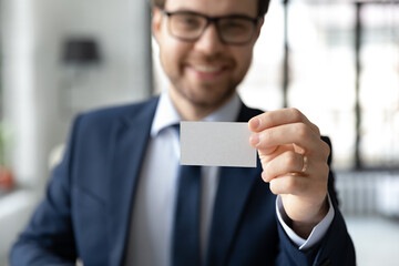 Close up confident businessman showing empty business card at camera, smiling executive manager demonstrating piece of paper with blank space, offering personal contact information to customer