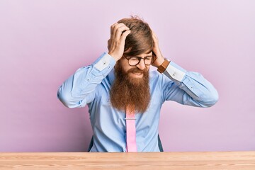 Wall Mural - Young irish redhead man wearing business shirt and tie sitting on the table suffering from headache desperate and stressed because pain and migraine. hands on head.